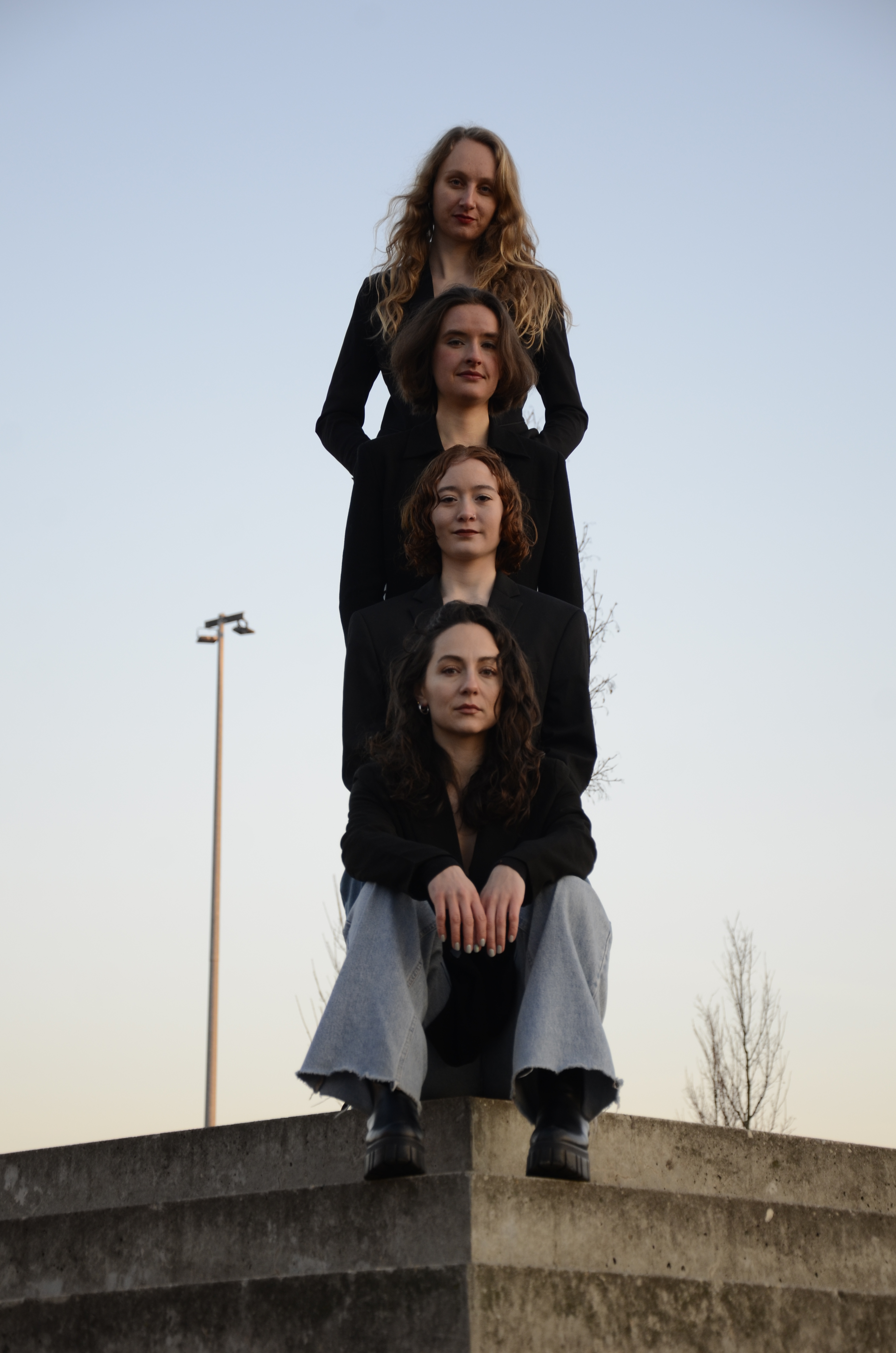 a portrait of the four artists wearing black shirts and jeans, standing in a row behind each other 