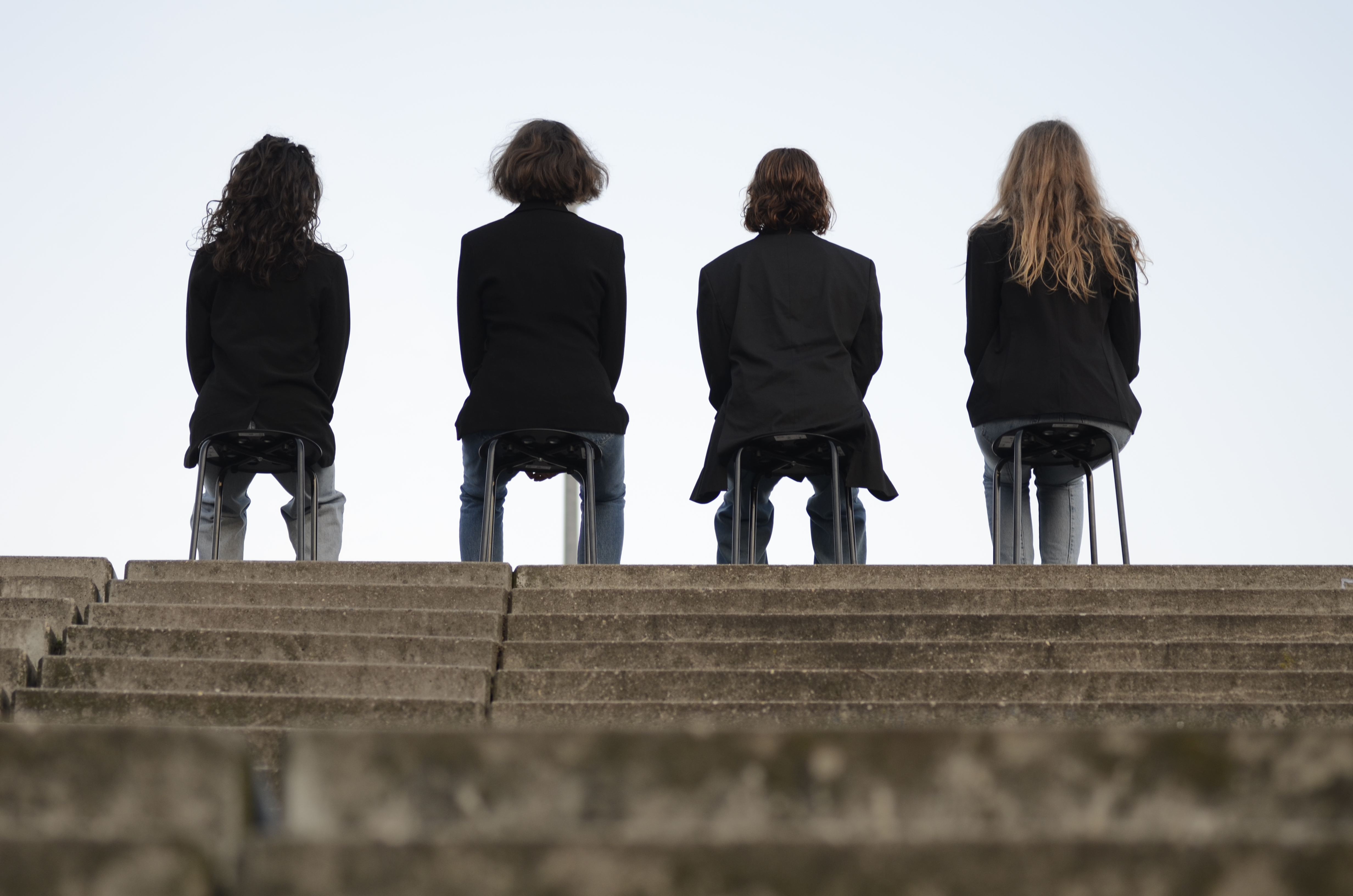 the four artists are sitting on small chairs on top of some concrete stairs with their backs turned to the viewer